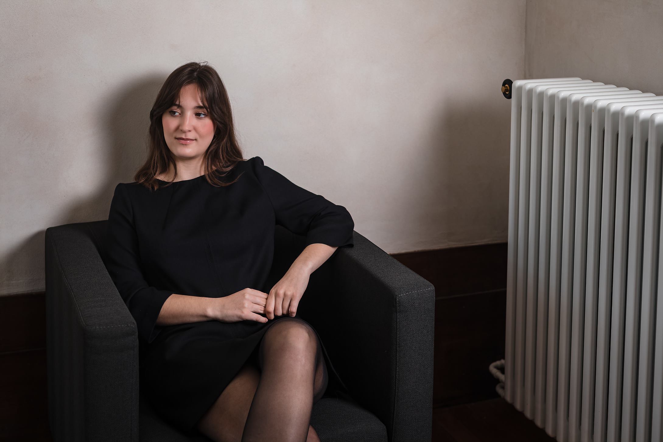 Une jeune femme assise sur un fauteuil dans une robe élégante Laurence Glorieux.